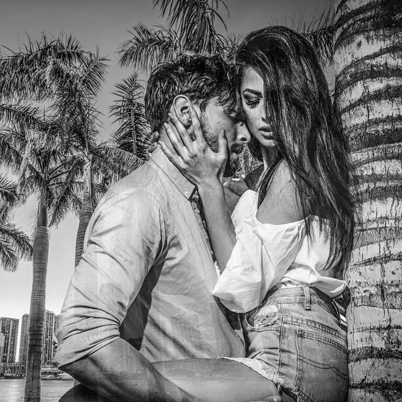 Romantic black and white photo of a shirtless man and woman in an embrace under blooming cherry blossoms.