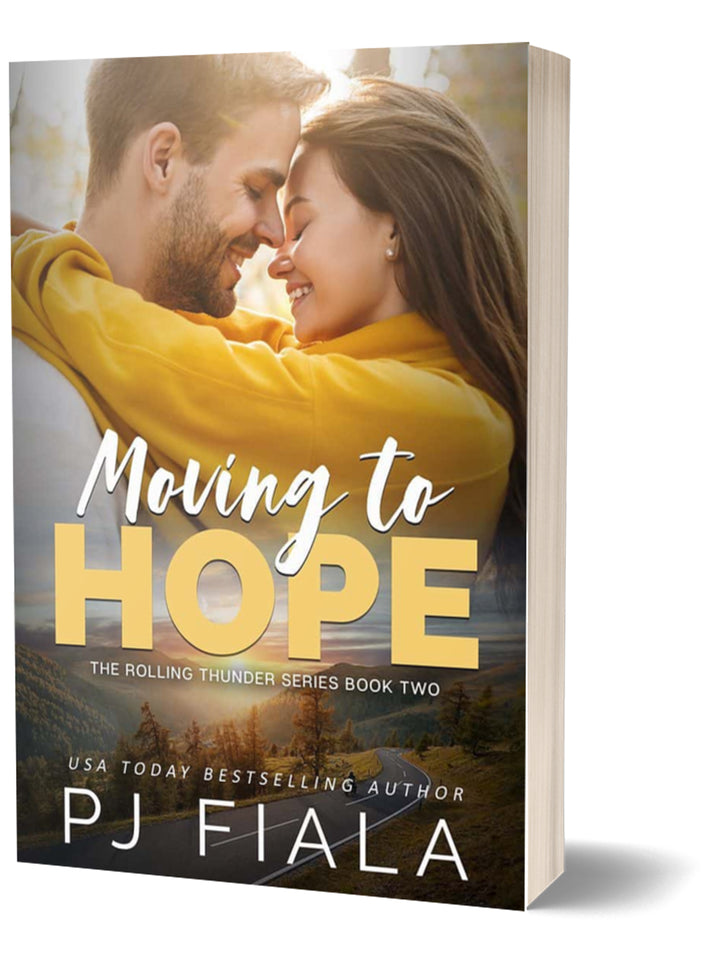 3D paperback edition of Moving to Hope by USA Today bestselling author PJ Fiala. A smiling couple wrapped together in a bright yellow blanket share an affectionate embrace above a scenic mountain landscape.