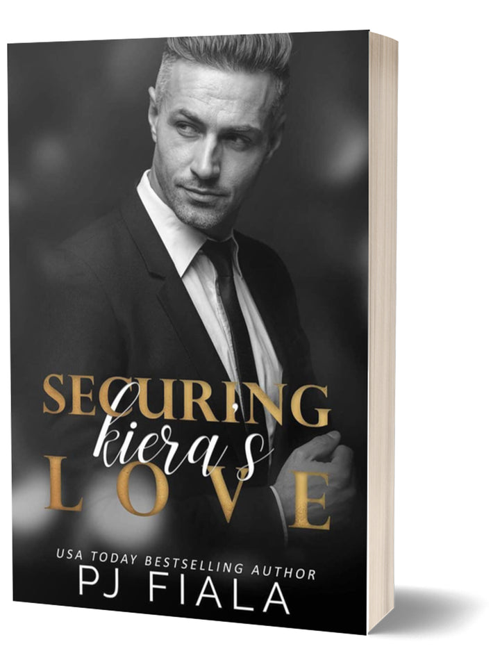 3D paperback edition of Securing Kiera's Love by USA Today bestselling author PJ Fiala. The cover features a distinguished silver-haired man in a tailored suit looking off to the side against a black-and-white backdrop, with the title in gold and white lettering for a polished contemporary romance design.